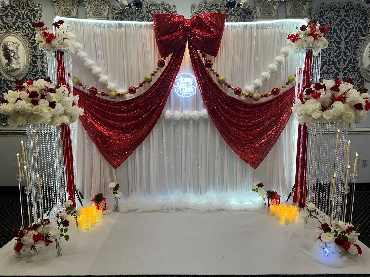 A New Year backdrop of white drapery swagged with red sequin fabric and a large red bow, with red and white roses and candles.