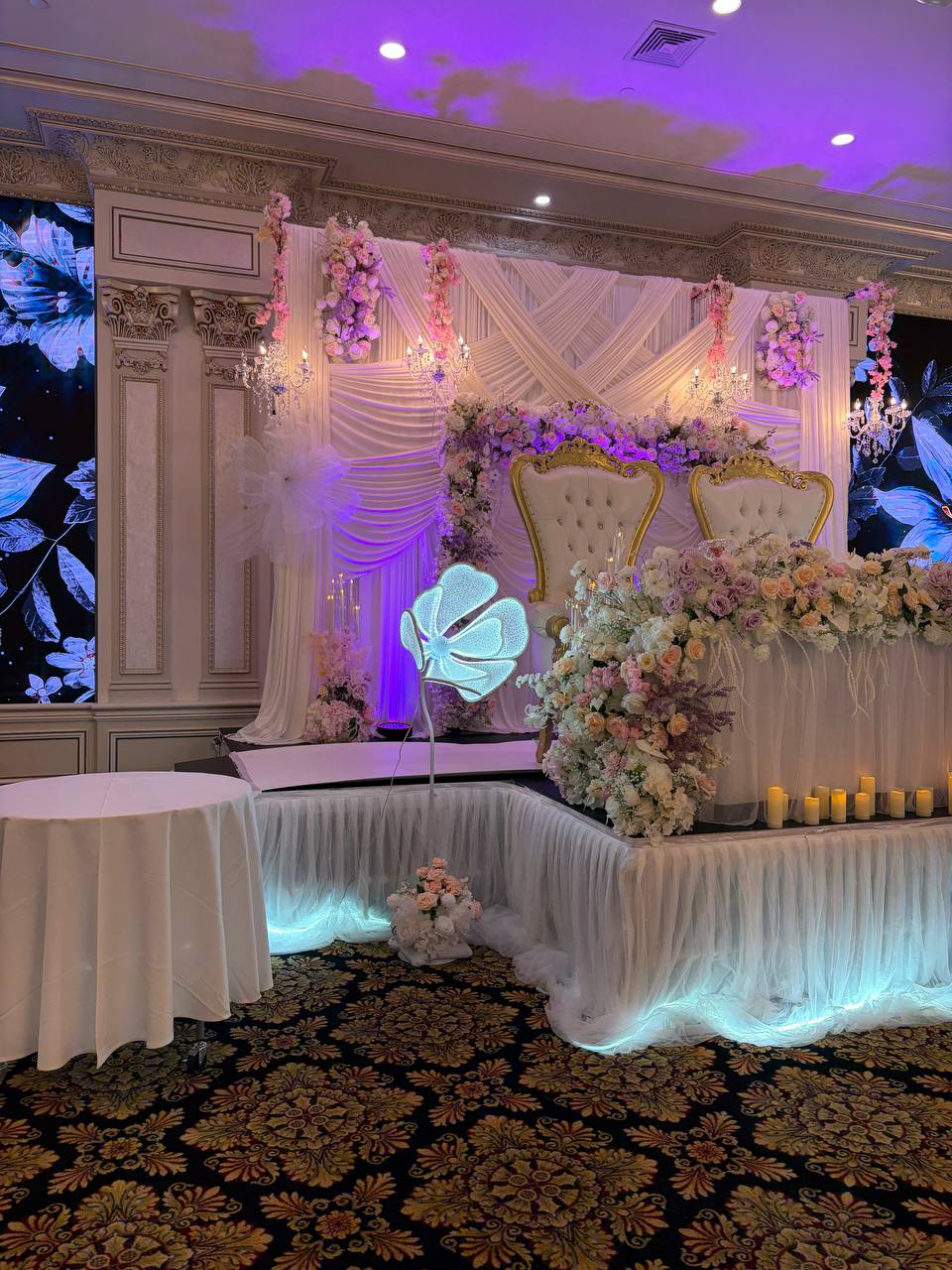 A wide view of a blush sweetheart table with gold thrones, a full floral runner and a tulle-skirted base lit from beneath.